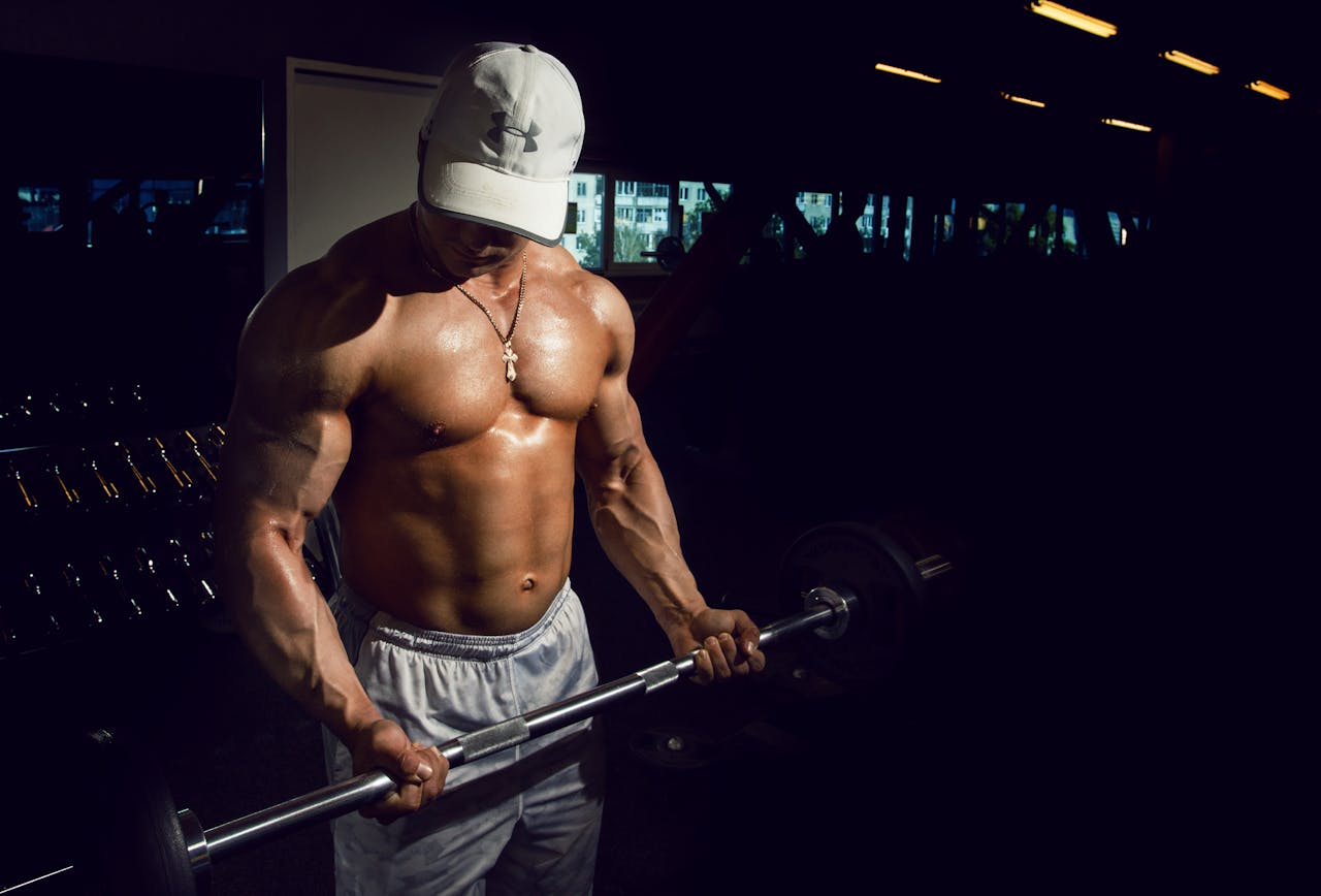our-story Strong shirtless man lifting barbell in a dimly lit gym, embodying fitness and strength.