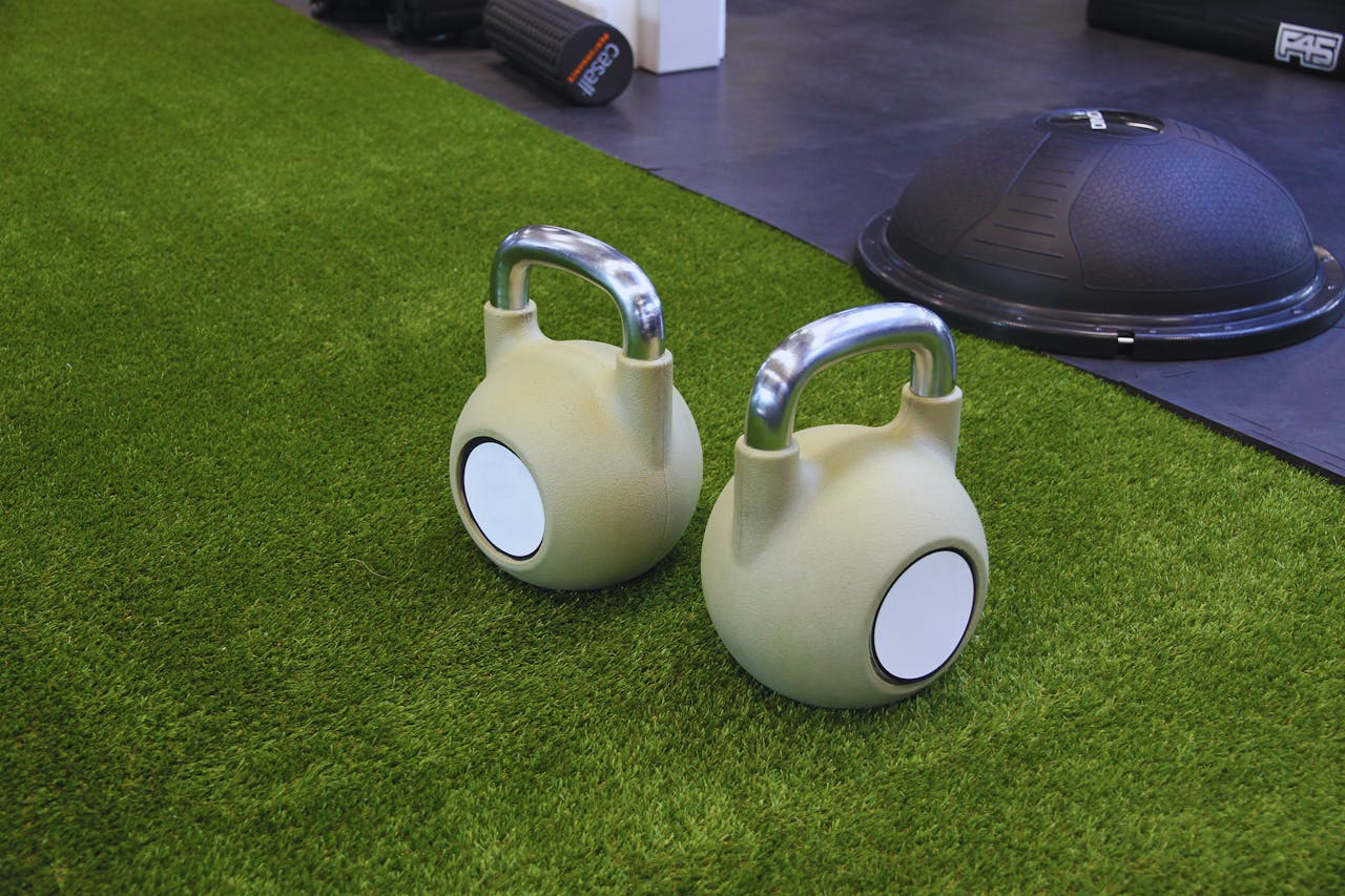 Two kettlebells on a green artificial grass floor in an indoor gym, ideal for strength training.
