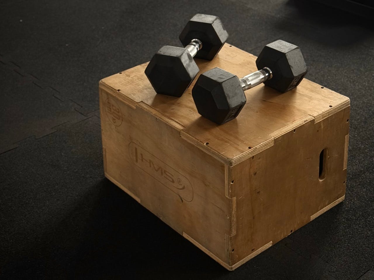 Pair of hex dumbbells on a wooden plyo box in a gym setting.