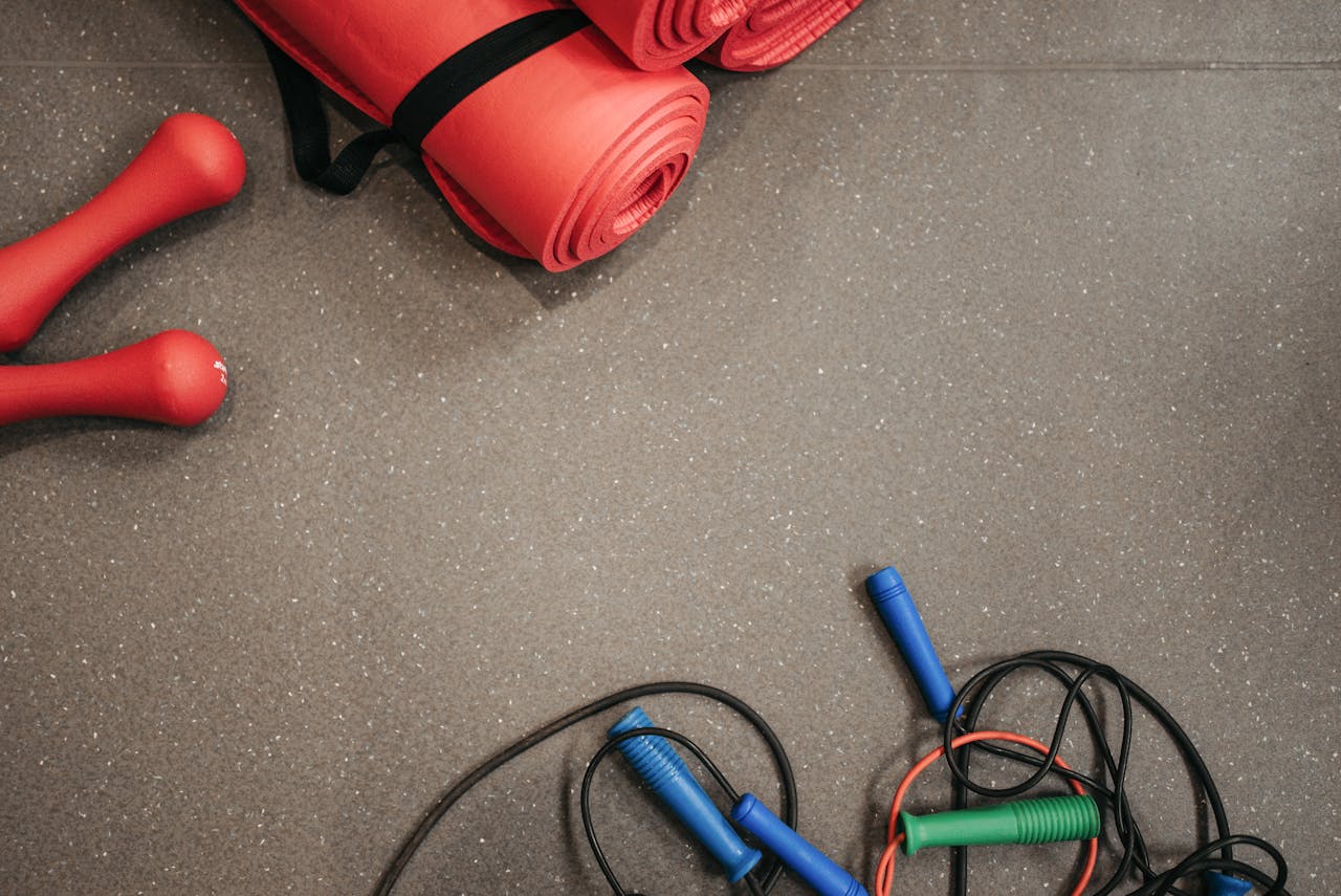 why-choose-us Red yoga mats, dumbbells, and jump ropes on a gym floor.