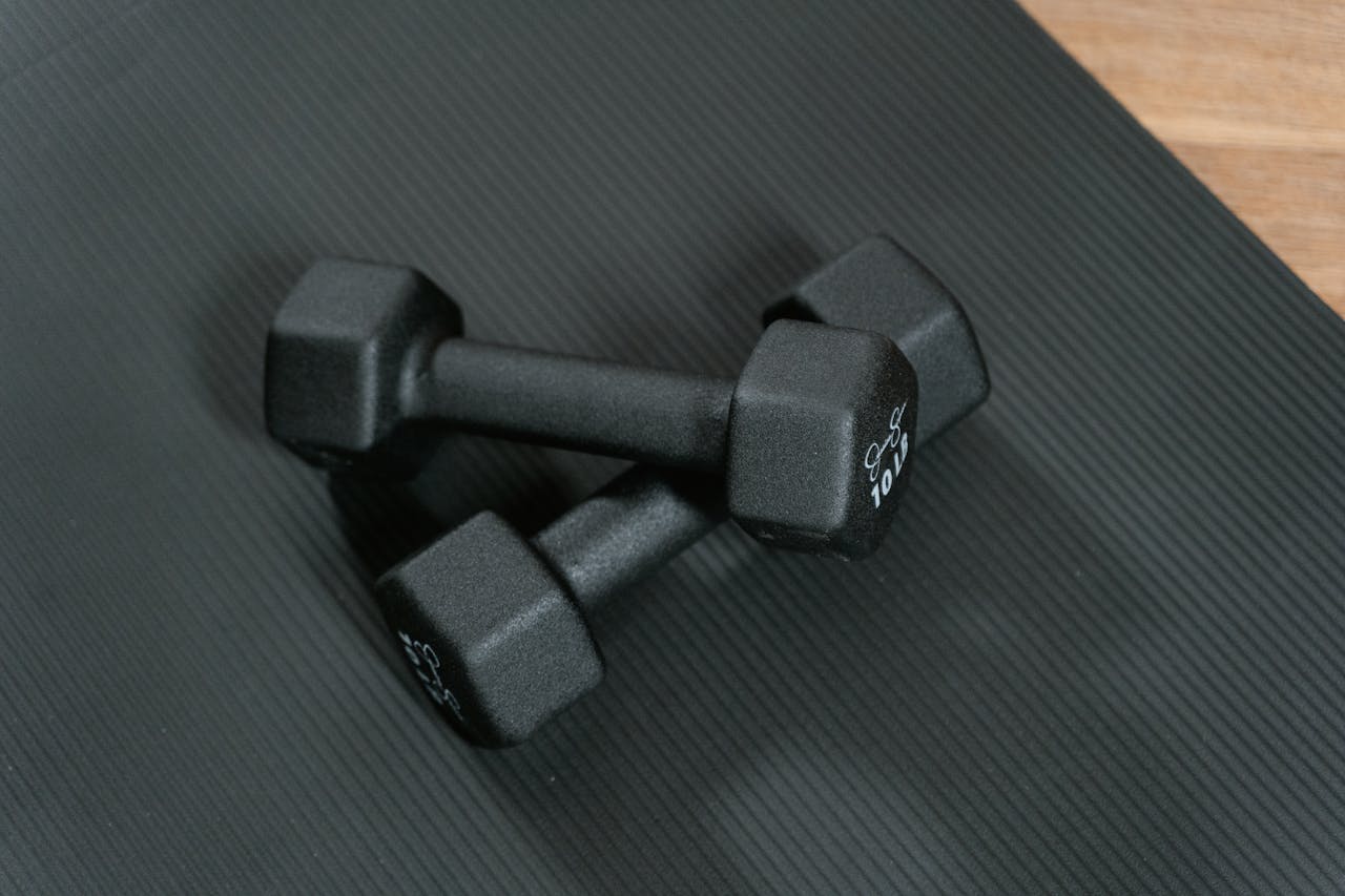 Black dumbbells placed on a yoga mat, perfect for home workouts and strength training.
