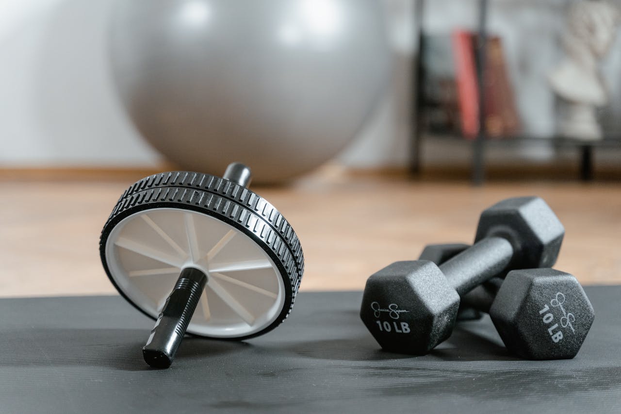 creative Close-up of ab wheel and dumbbells on a mat in a home gym setting.